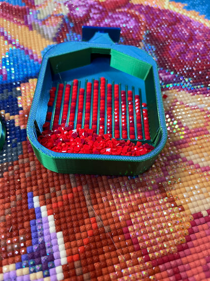 Small green Deluxe 2 Phoenix diamond painting tray with red drill pieces on colorful canvas background.