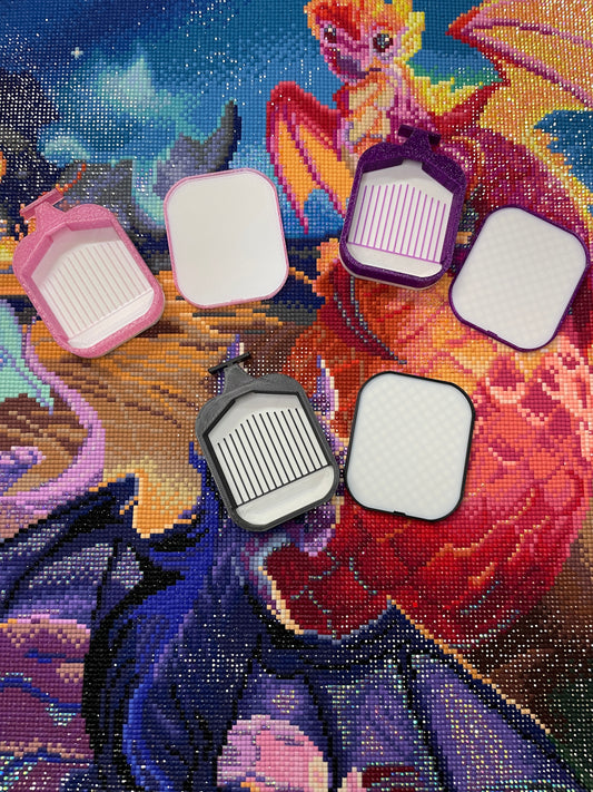 Colorful small diamond painting trays with white bases and various lids on a vibrant dragon background