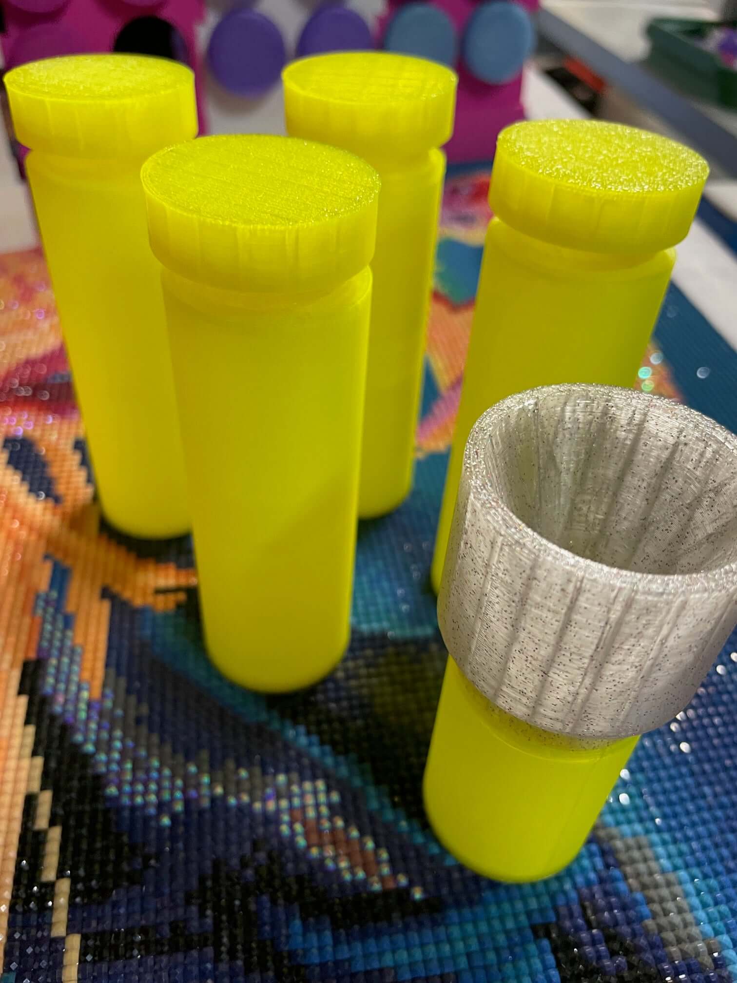 Yellow TestToobz Drill Containers with screw-on funnel on a decorative surface.