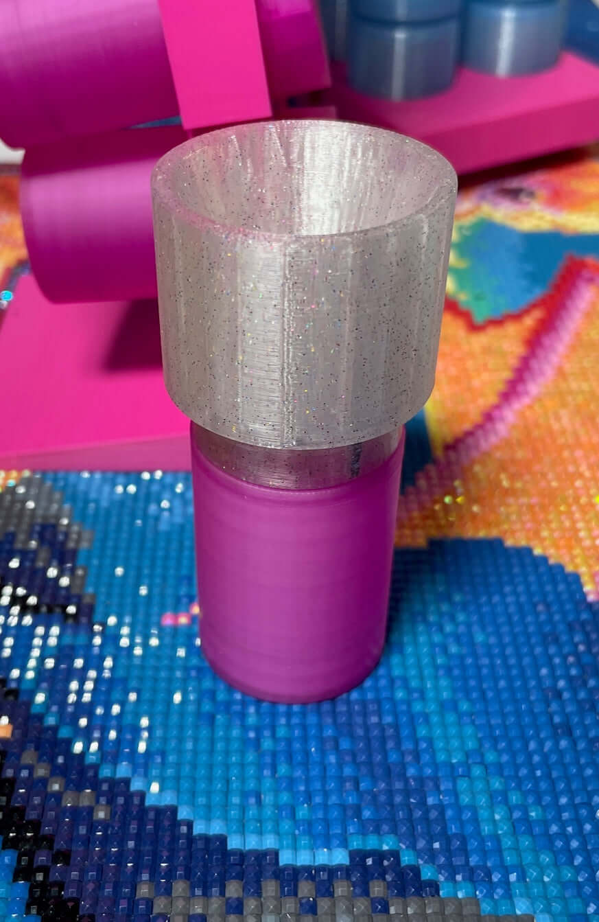 Pink expandable drill container with a screw-on funnel, displayed on a colorful craft mat.