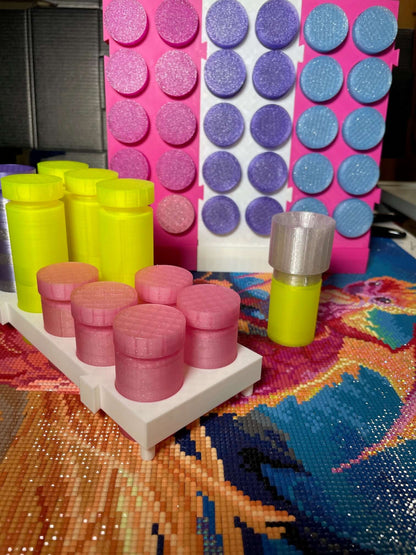 Colorful drill containers with expandable stand on a craft table, featuring pink, yellow, and purple containers in packs of ten.